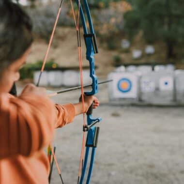 Focused young woman aiming a bow at an archery target in an outdoor range.